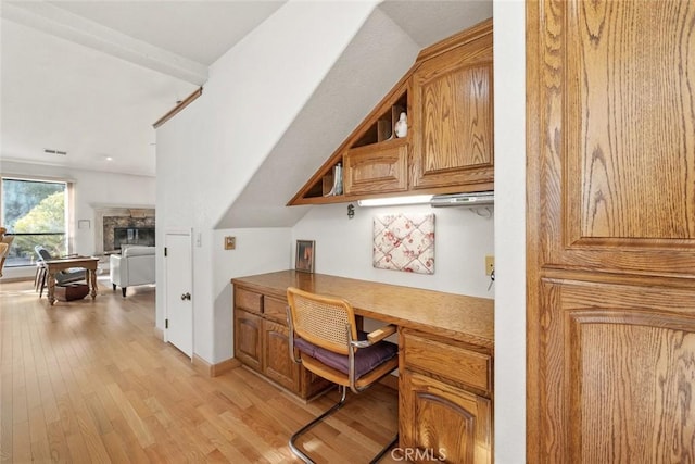 home office with built in study area, baseboards, a glass covered fireplace, and light wood-type flooring