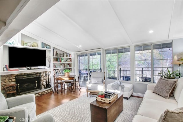 living room featuring lofted ceiling, hardwood / wood-style floors, built in shelves, and a stone fireplace