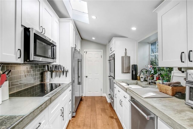 kitchen featuring appliances with stainless steel finishes, sink, white cabinets, decorative backsplash, and light hardwood / wood-style floors