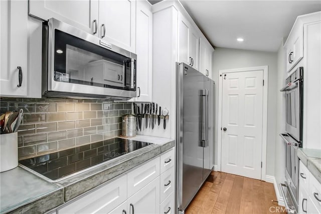 kitchen with white cabinets, backsplash, light stone counters, stainless steel appliances, and light hardwood / wood-style flooring