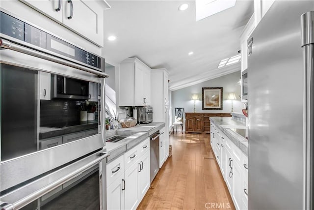 kitchen with vaulted ceiling, light hardwood / wood-style flooring, appliances with stainless steel finishes, decorative backsplash, and white cabinets