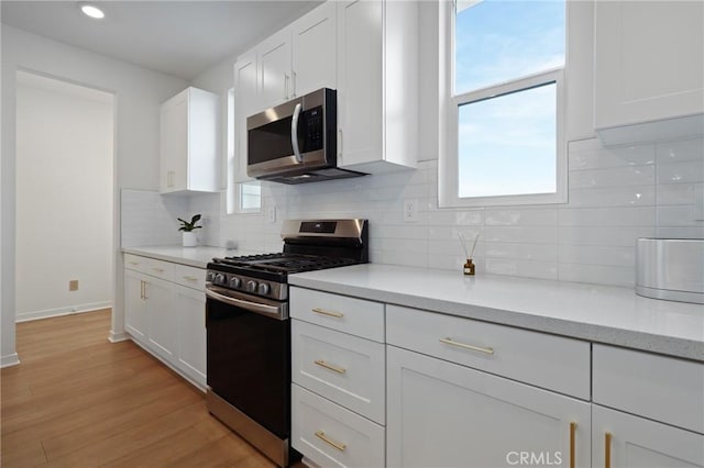 kitchen with light hardwood / wood-style flooring, appliances with stainless steel finishes, tasteful backsplash, light stone countertops, and white cabinets