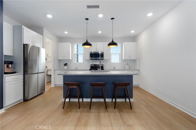 kitchen featuring white cabinetry, hanging light fixtures, a center island with sink, stainless steel appliances, and backsplash