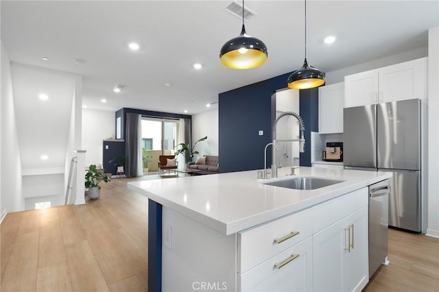 kitchen with an island with sink, sink, white cabinets, hanging light fixtures, and stainless steel appliances