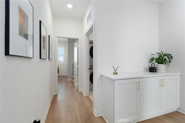 hallway featuring stacked washer / dryer and light hardwood / wood-style flooring