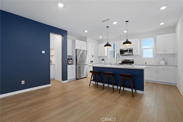 kitchen with white cabinetry, appliances with stainless steel finishes, a center island with sink, and decorative light fixtures