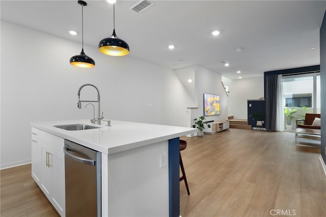 kitchen featuring pendant lighting, white cabinetry, sink, stainless steel dishwasher, and a center island with sink