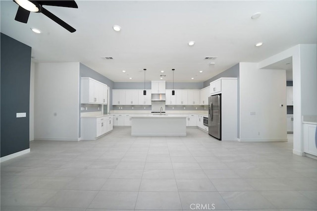 kitchen featuring pendant lighting, sink, white cabinets, stainless steel refrigerator with ice dispenser, and a center island with sink