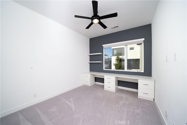 interior space featuring light carpet, built in desk, and ceiling fan