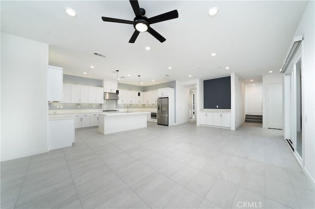 kitchen with sink, stainless steel fridge, white cabinets, a kitchen island, and decorative light fixtures