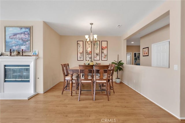 dining space with a chandelier, a glass covered fireplace, visible vents, and light wood-style floors