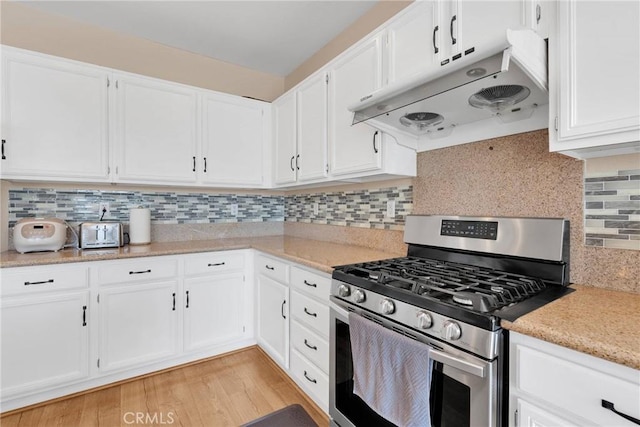 kitchen with white cabinets, stainless steel gas stove, under cabinet range hood, and light wood finished floors