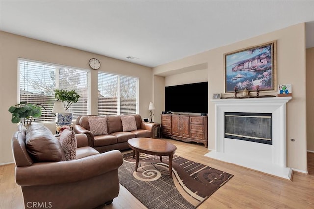 living area with a glass covered fireplace, visible vents, and light wood finished floors