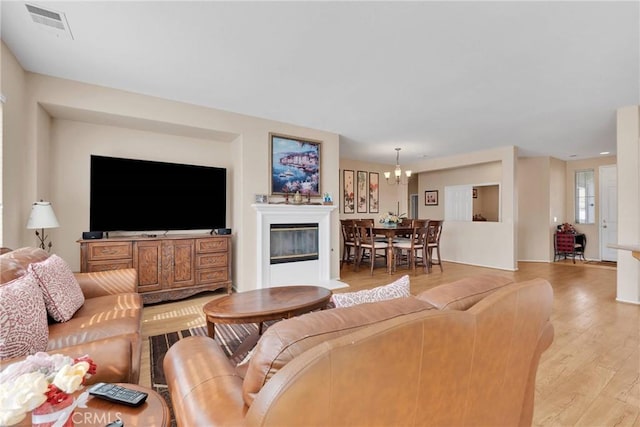 living room featuring light wood-type flooring, an inviting chandelier, visible vents, and a glass covered fireplace