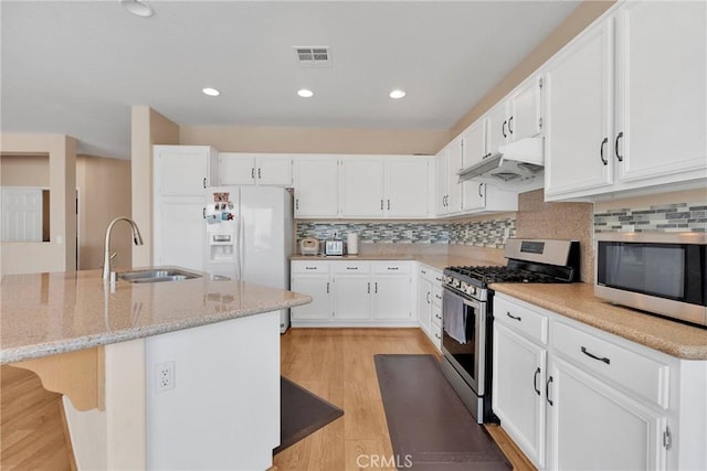 kitchen featuring under cabinet range hood, stainless steel appliances, a sink, visible vents, and light stone countertops