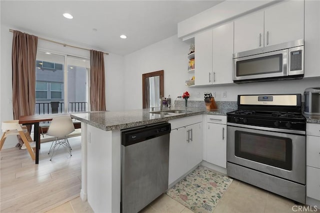 kitchen featuring appliances with stainless steel finishes, sink, white cabinets, dark stone counters, and kitchen peninsula