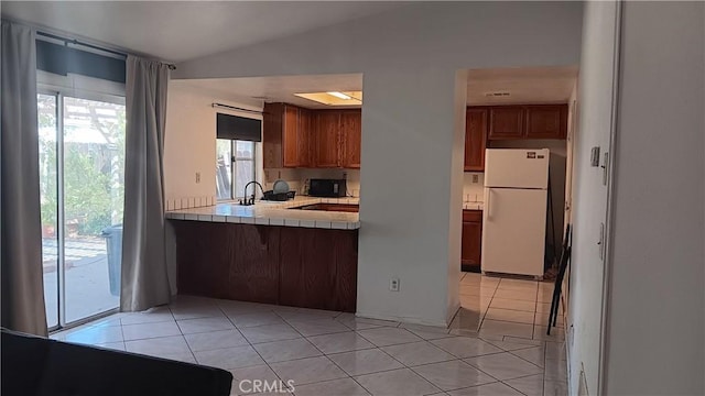 kitchen featuring lofted ceiling, light tile patterned floors, white refrigerator, tile counters, and kitchen peninsula