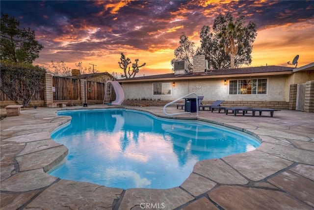 pool at dusk with a patio area, a fenced in pool, a water slide, and fence