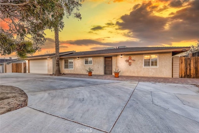 ranch-style home featuring fence, a garage, driveway, and stucco siding