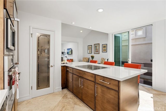 kitchen featuring a breakfast bar area, stainless steel oven, black electric stovetop, light tile patterned floors, and kitchen peninsula