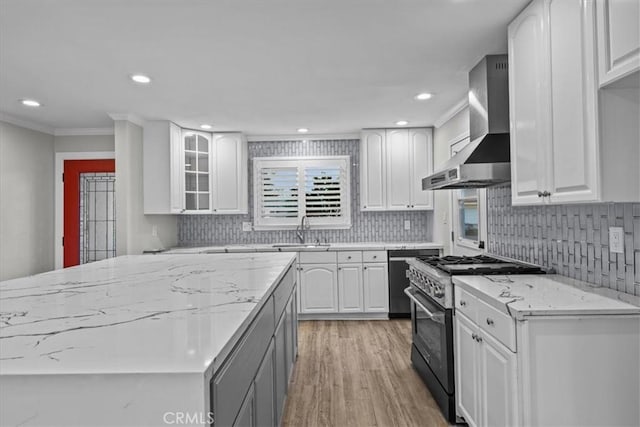 kitchen featuring white cabinetry, sink, high end stainless steel range oven, light stone counters, and wall chimney exhaust hood