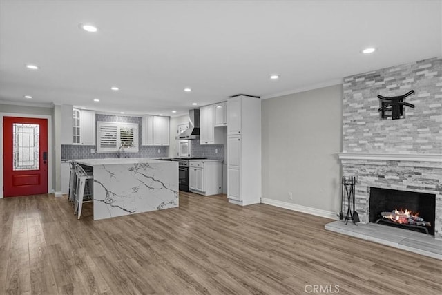 kitchen with wall chimney exhaust hood, a kitchen bar, stainless steel range oven, white cabinetry, and a center island