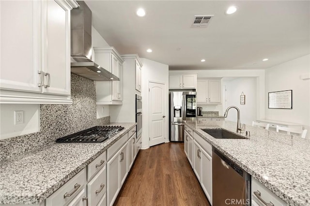 kitchen featuring sink, white cabinets, stainless steel appliances, light stone countertops, and wall chimney range hood