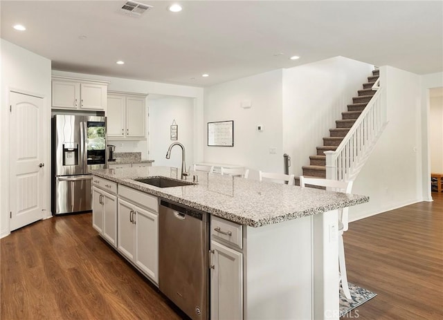 kitchen with appliances with stainless steel finishes, an island with sink, sink, a kitchen bar, and light stone counters