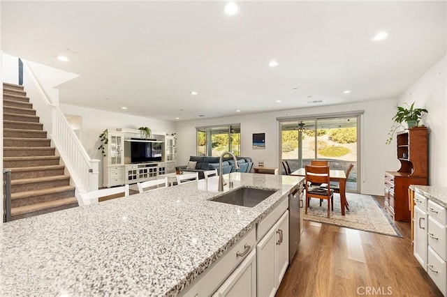 kitchen with sink, stainless steel dishwasher, light stone countertops, hardwood / wood-style floors, and white cabinets