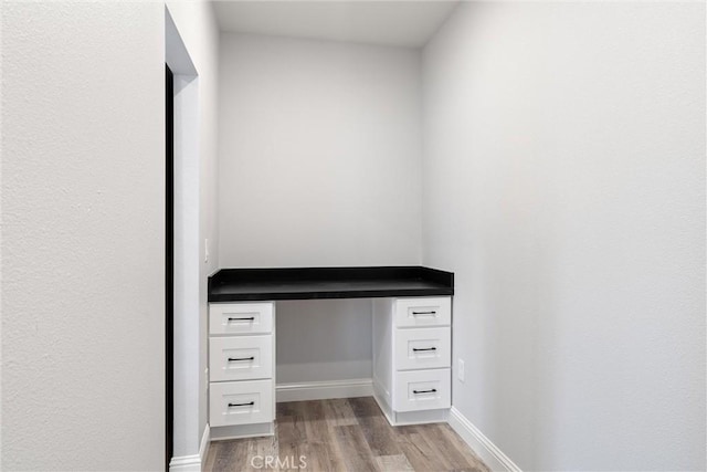 unfurnished office featuring built in desk and light wood-type flooring