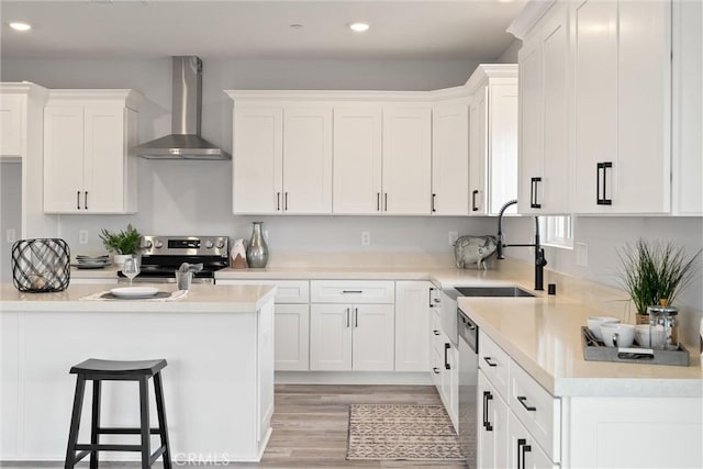 kitchen featuring appliances with stainless steel finishes, sink, white cabinets, wall chimney range hood, and light hardwood / wood-style flooring