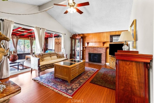 living room with a fireplace, vaulted ceiling with beams, hardwood / wood-style flooring, ceiling fan, and a textured ceiling