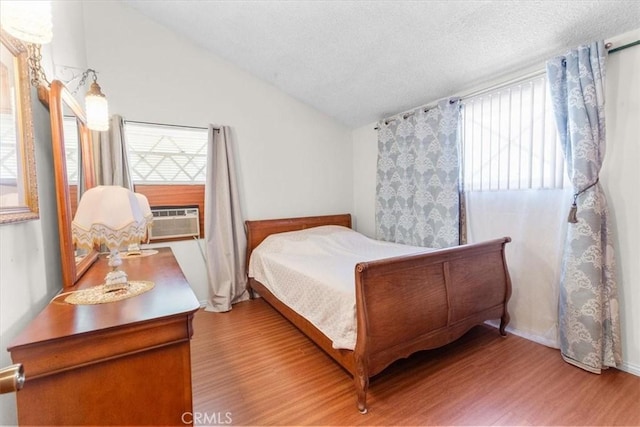 bedroom featuring vaulted ceiling, cooling unit, a textured ceiling, and light wood-type flooring