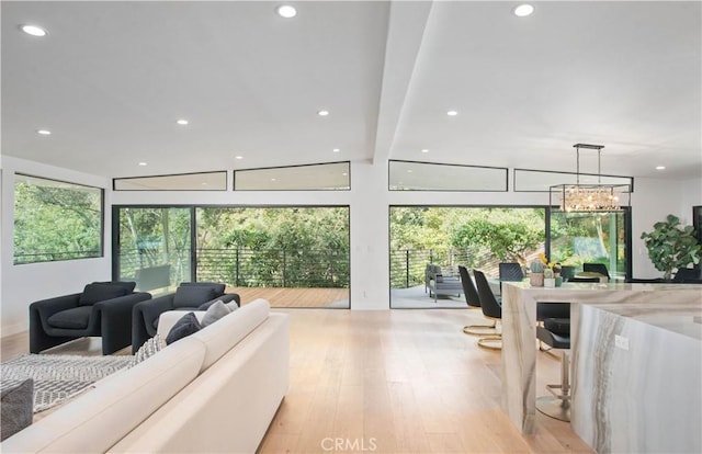 living room with a notable chandelier, beam ceiling, and light hardwood / wood-style flooring