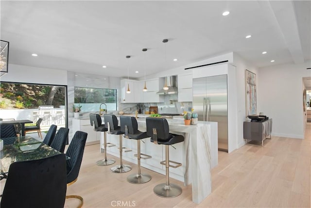 kitchen featuring pendant lighting, tasteful backsplash, light hardwood / wood-style floors, white cabinets, and wall chimney exhaust hood