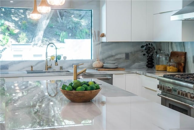 kitchen featuring high end stainless steel range oven, white cabinetry, hanging light fixtures, decorative backsplash, and wall chimney exhaust hood