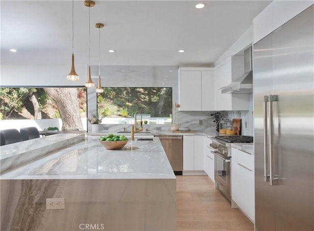 kitchen featuring wall chimney exhaust hood, sink, decorative light fixtures, high quality appliances, and white cabinets