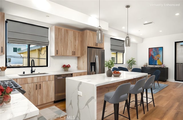 kitchen featuring sink, appliances with stainless steel finishes, a center island, light stone countertops, and decorative light fixtures