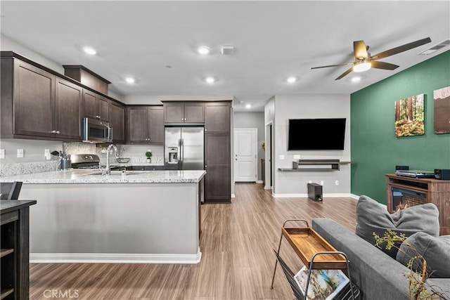 kitchen with light stone counters, dark brown cabinetry, stainless steel appliances, a sink, and open floor plan