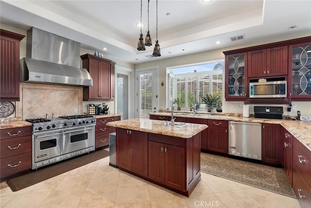 kitchen with appliances with stainless steel finishes, wall chimney exhaust hood, recessed lighting, tasteful backsplash, and a tray ceiling