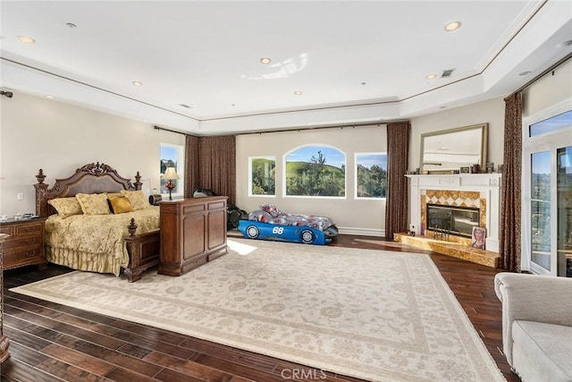 bedroom featuring a high end fireplace, a raised ceiling, and wood finished floors