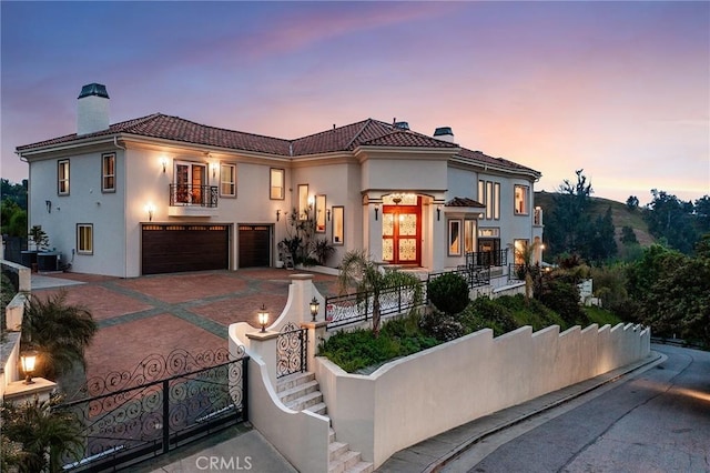 mediterranean / spanish-style home with a tiled roof, a fenced front yard, a chimney, a garage, and a balcony