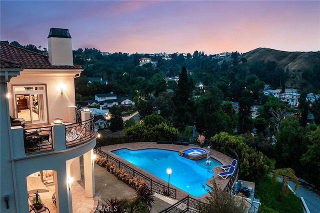 pool at dusk featuring a pool with connected hot tub and a patio area