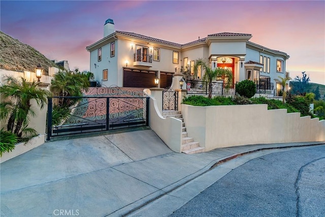 mediterranean / spanish house featuring a fenced front yard, an attached garage, stucco siding, a gate, and a chimney