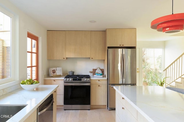 kitchen featuring pendant lighting, light stone counters, stainless steel appliances, light brown cabinets, and light hardwood / wood-style flooring