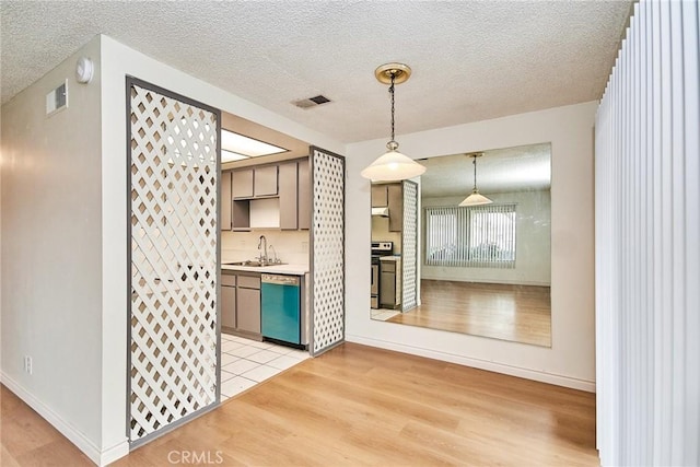 kitchen with sink, light wood-type flooring, a textured ceiling, decorative light fixtures, and stainless steel appliances