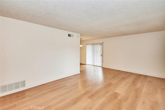 empty room with light wood-type flooring and a textured ceiling