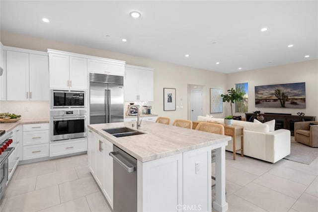 kitchen featuring sink, white cabinetry, a kitchen island with sink, built in appliances, and a kitchen bar