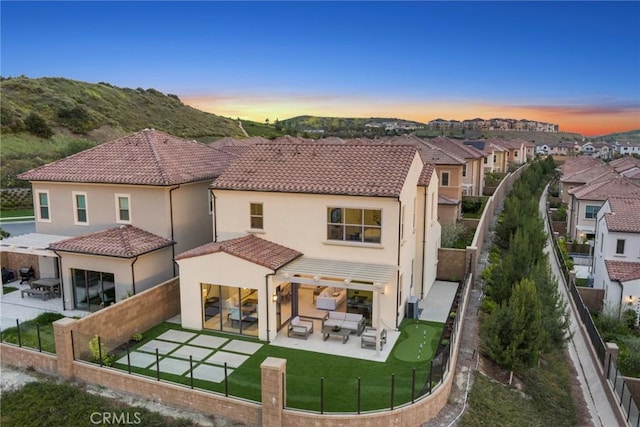 back house at dusk with outdoor lounge area, a patio area, and a lawn