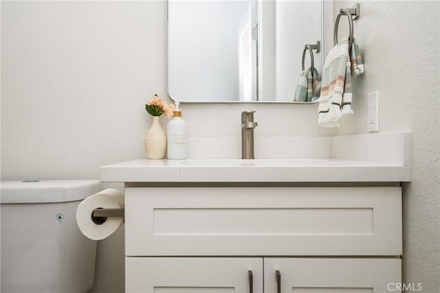 bathroom with toilet, a textured wall, and vanity